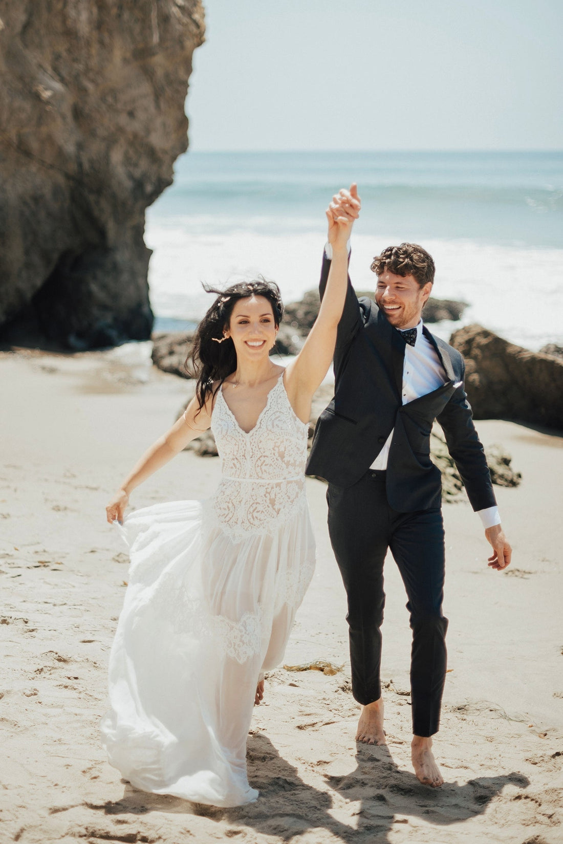 Bohemian lace wedding dress with thin straps, lace bodice and flowing chiffon skirt by Lace & Love by Shany Sasson, worn by a bride at a beach wedding.