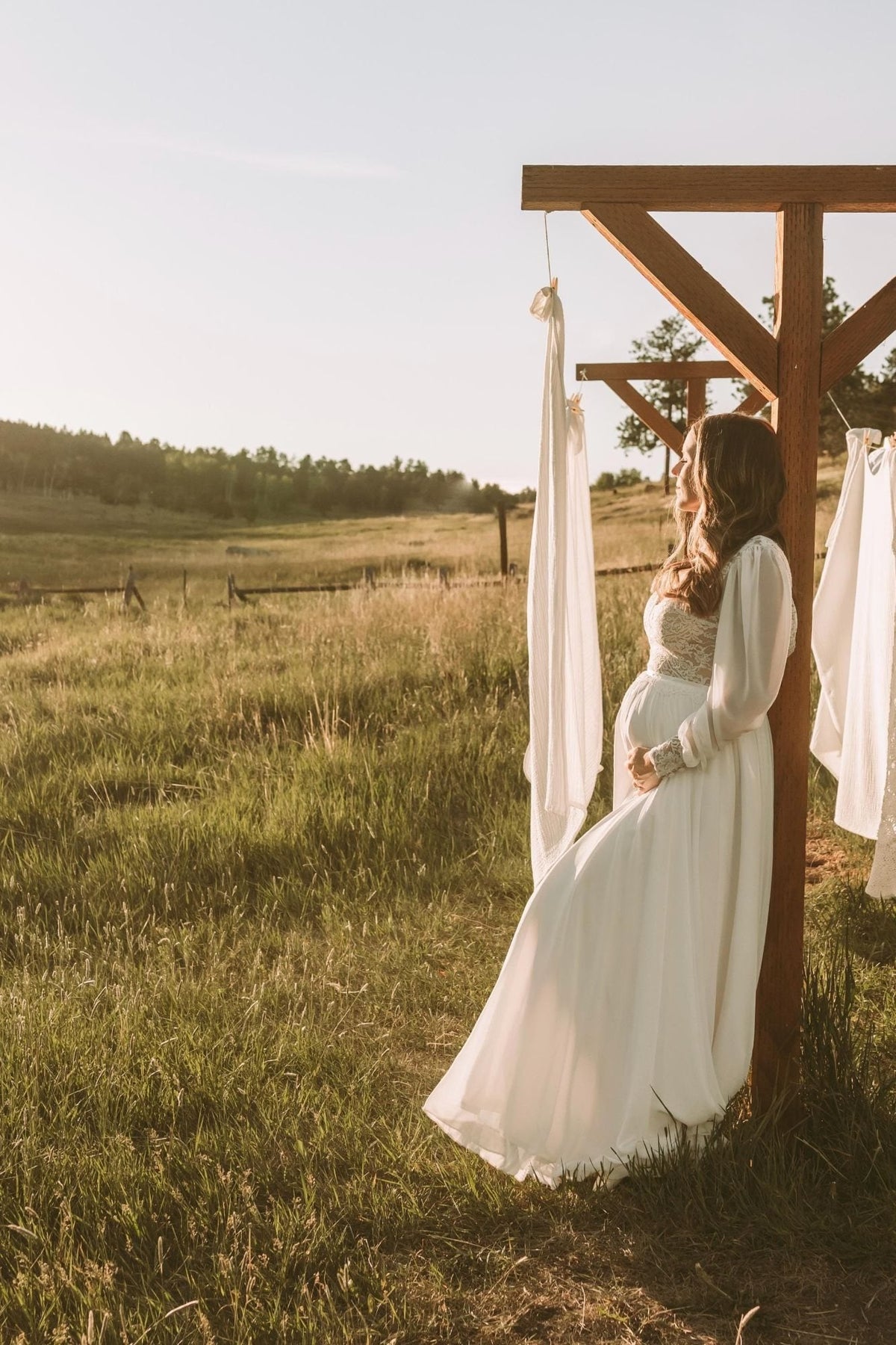 Emily at 32 weeks pregnant in the Diana gown by Lace & Love, a lace bodice with sheer chiffon sleeves and a flowing chiffon skirt, in a meadow at sunset