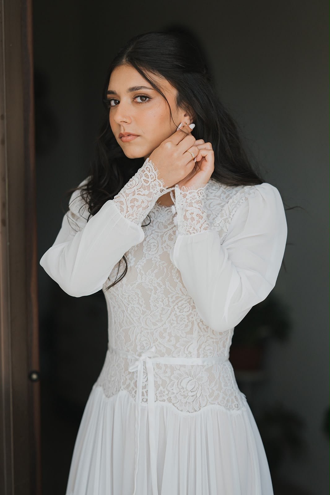 A bride in a modest boho wedding dress by Lace & Love: a high lace neckline, long chiffon sleeves with lace cuffs and a ribbon tie at the waist