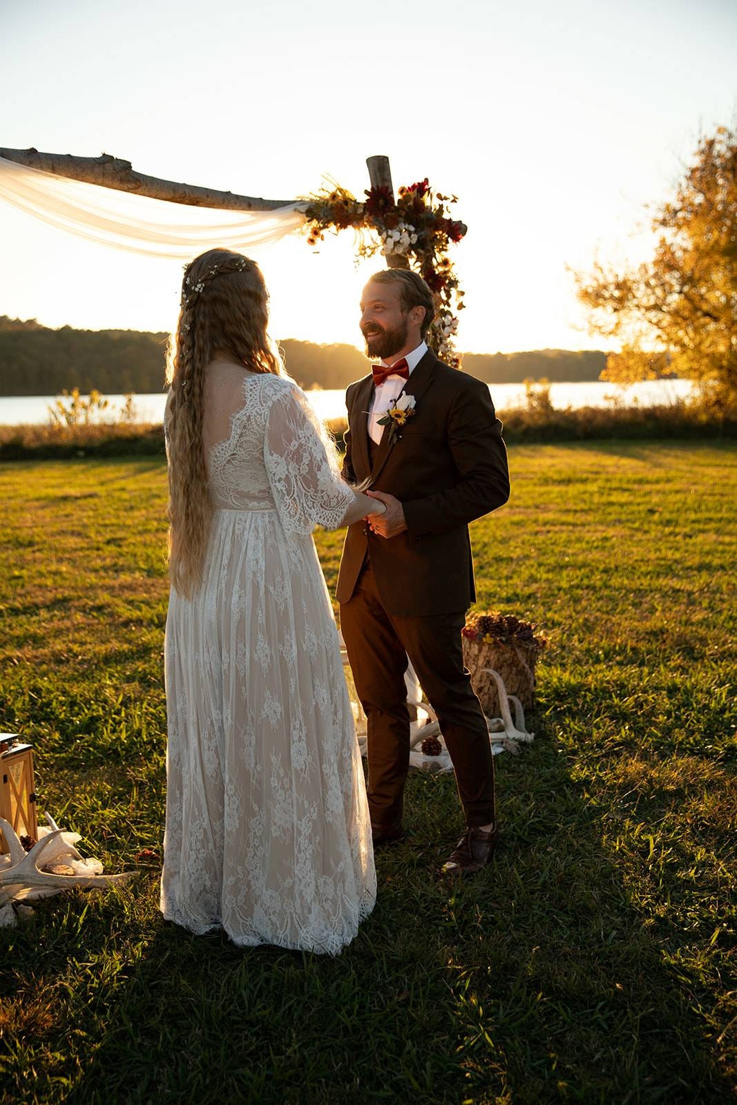 Bride wearing a boho lace wedding dress standing with her groom during a romantic sunset wedding ceremony.