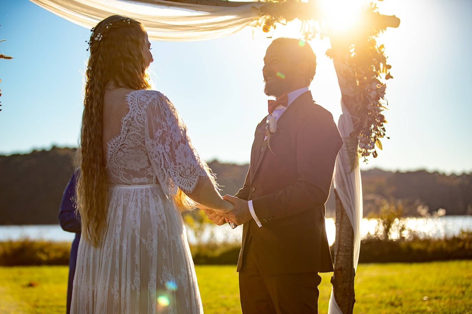 Romantic bride in a boho wedding dress standing with her groom at sunset.