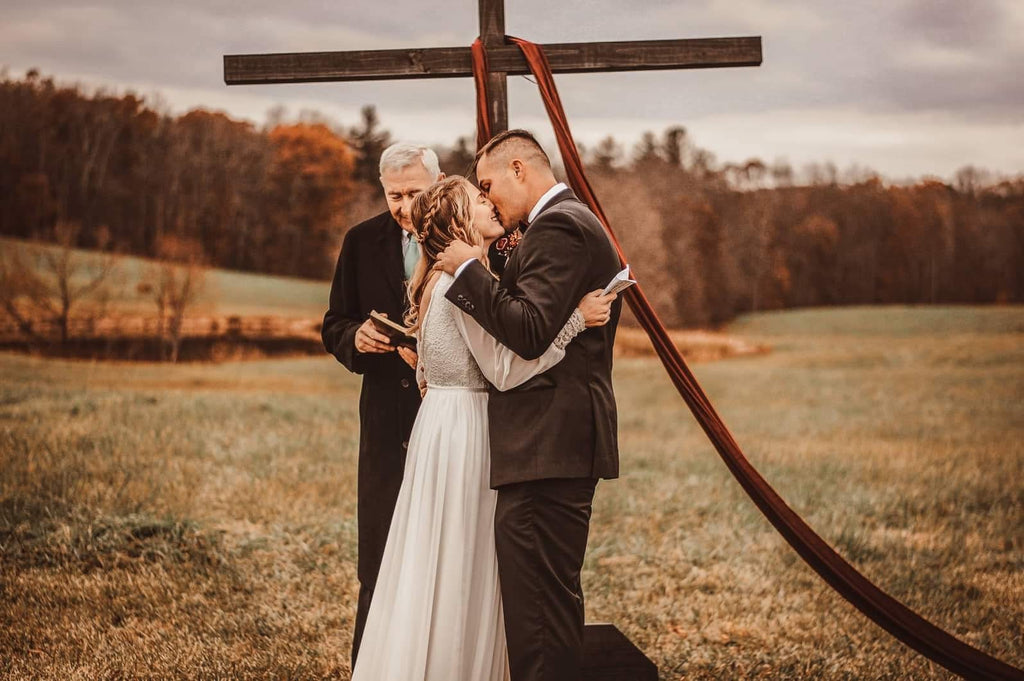 Bride and groom standing beneath a rustic wedding arch during their boho outdoor ceremony.