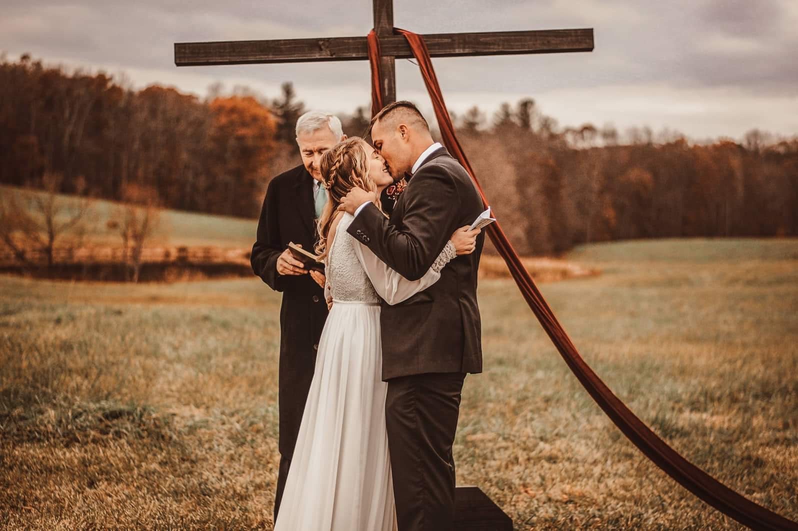 Bride and groom standing beneath a rustic wedding arch during their boho outdoor ceremony.
